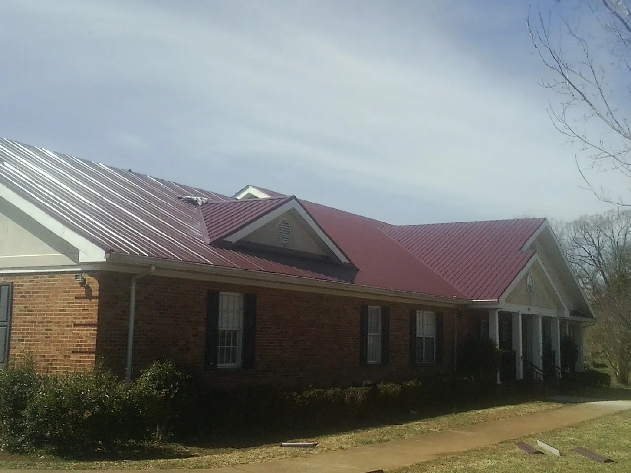 Red metal roof with gabled entries on a long brick building, from a Hail Damage Roof Repair job in Bumpass