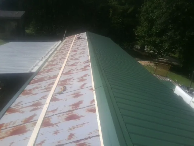 Old rusted panels beside newly installed green metal roofing — Wind Damage Roof Repair by Roofing Brothers in Bumpass