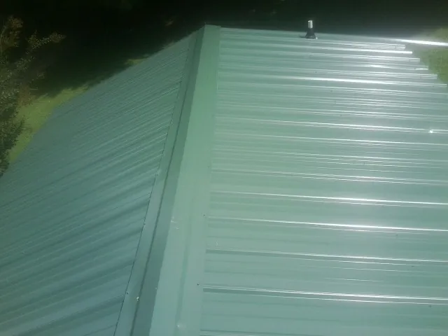 New green metal panels meeting at the ridge of a roof — Flat Roof Repair work by our crew in Bumpass