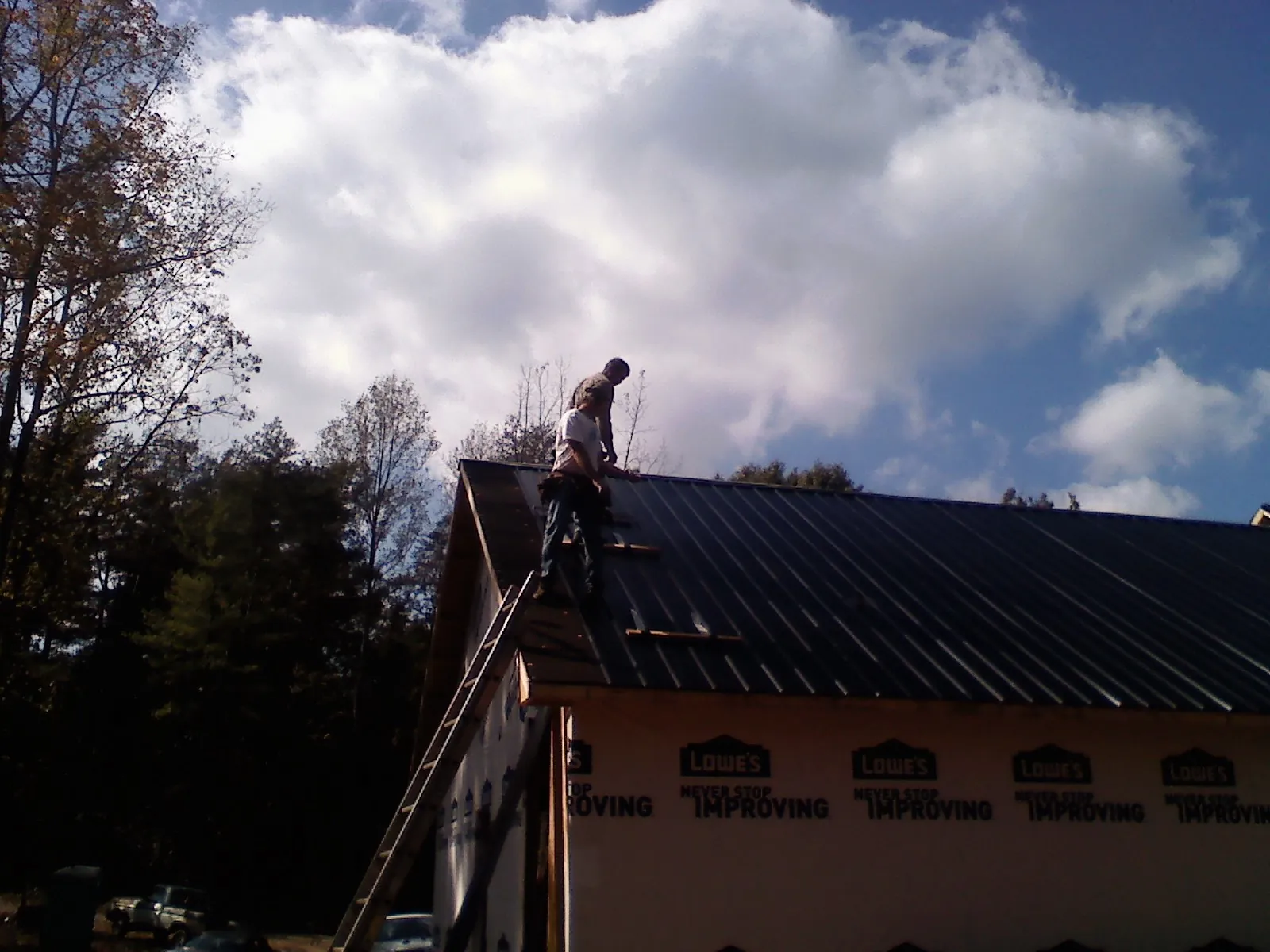 Roofer fastening dark metal panels high against a cloudy sky, from a Roof Inspection job in Bumpass